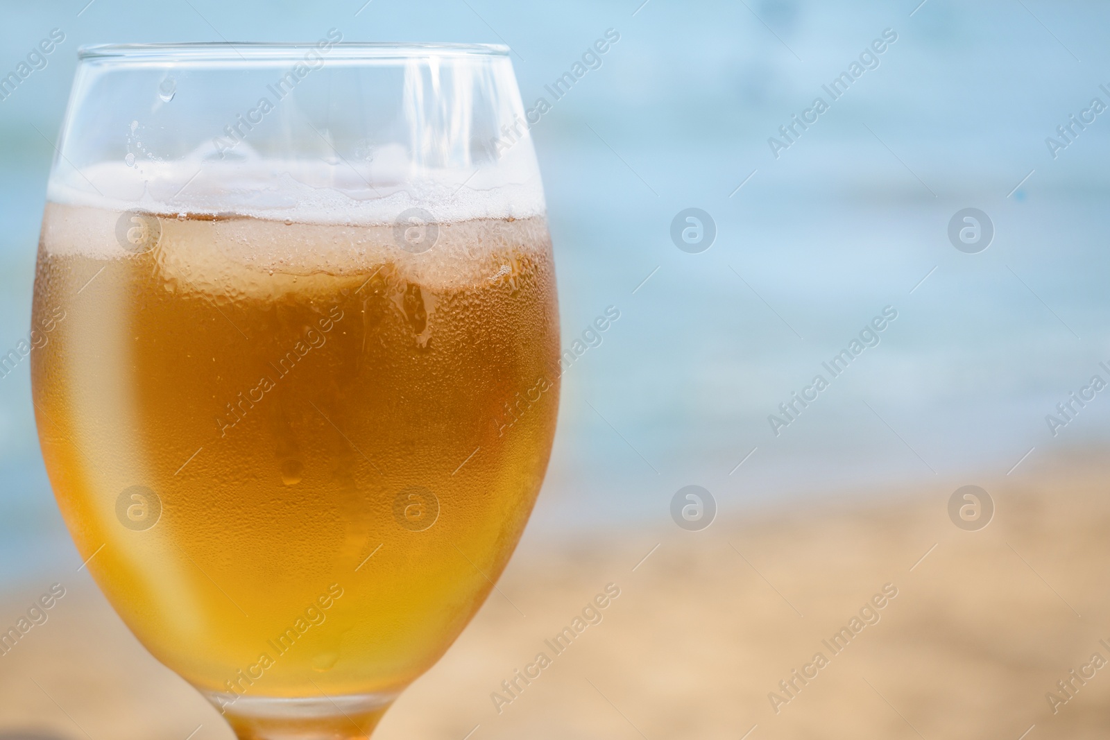 Photo of Cold beer in glass on beach, closeup. Space for text