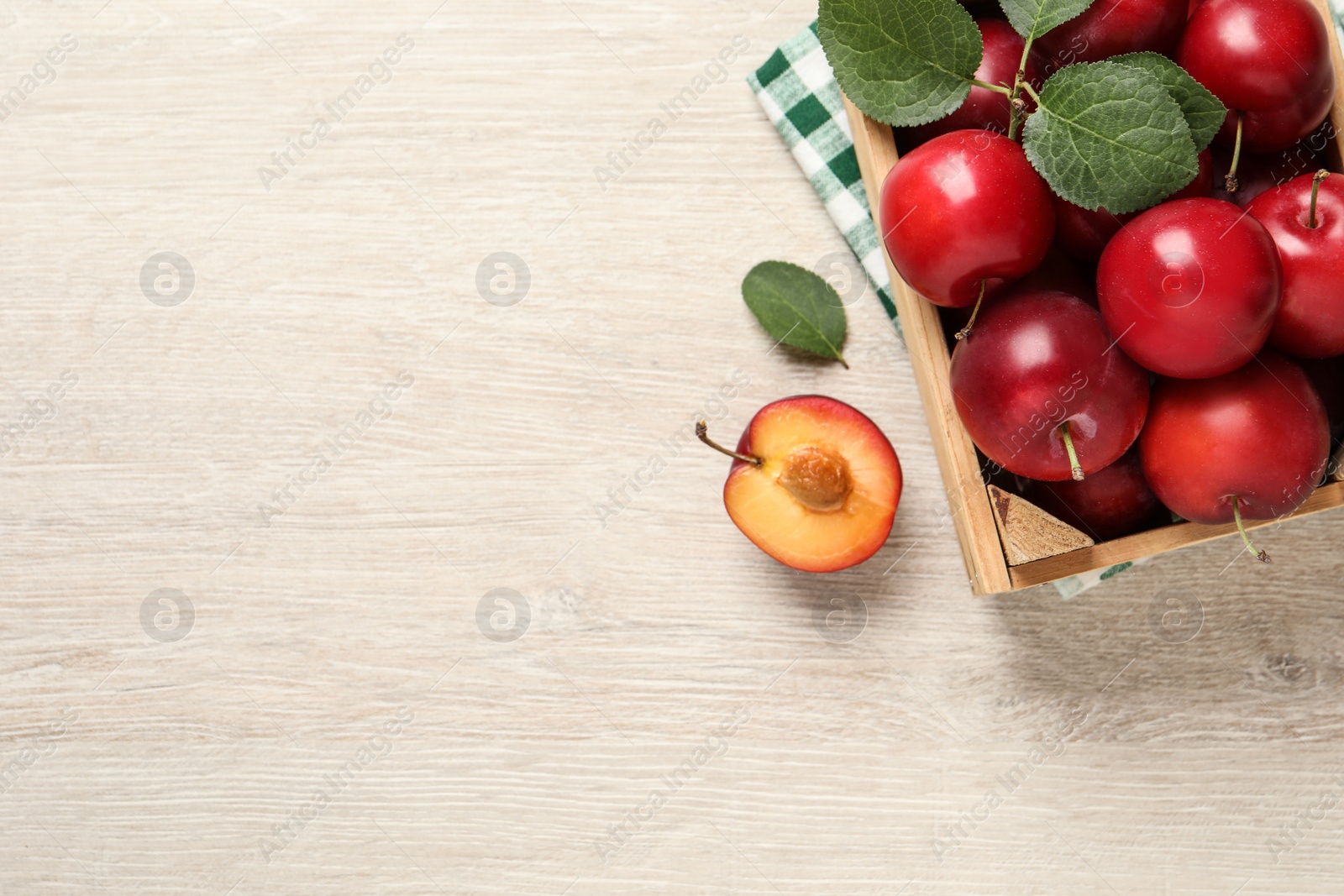 Photo of Delicious ripe cherry plums with leaves on white wooden table, flat lay. Space for text