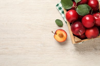 Photo of Delicious ripe cherry plums with leaves on white wooden table, flat lay. Space for text