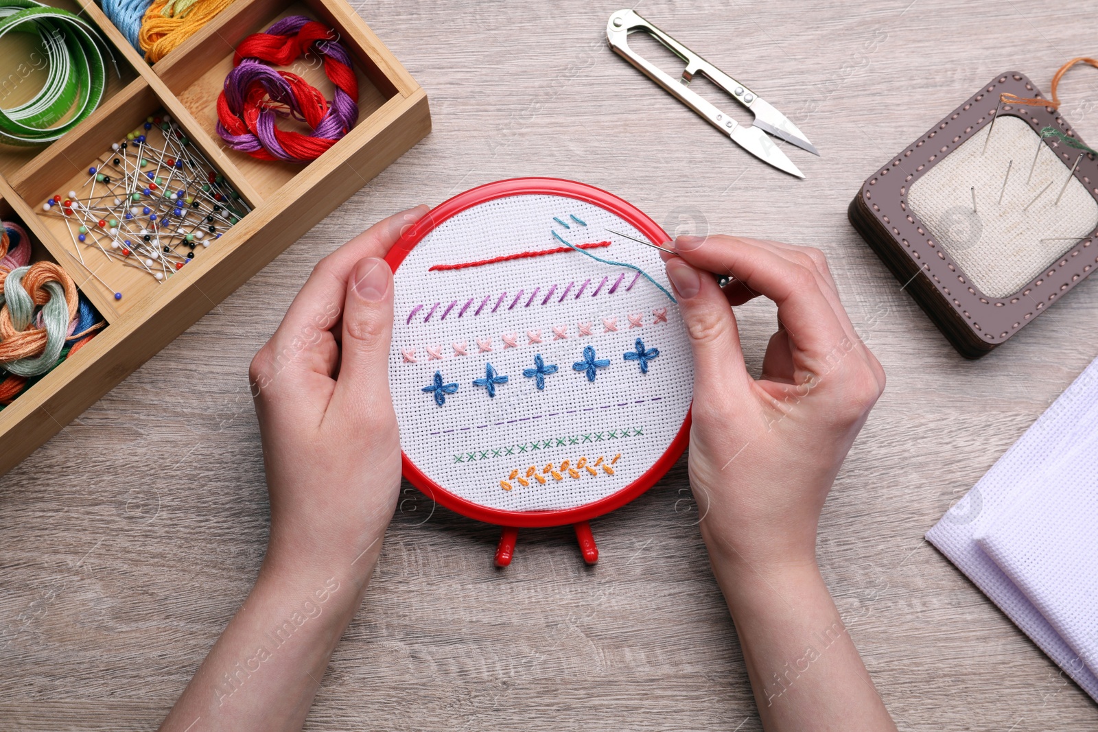 Photo of Woman doing different stitches with colorful threads on fabric in embroidery hoop at wooden table, top view