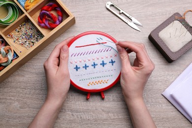 Photo of Woman doing different stitches with colorful threads on fabric in embroidery hoop at wooden table, top view