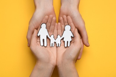 Photo of Couple holding paper family cutout on yellow background, top view