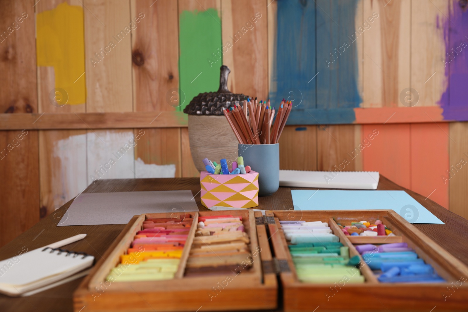 Photo of Blank sheets of paper, colorful chalk pastels and drawing pencils on wooden table indoors. Modern artist's workplace