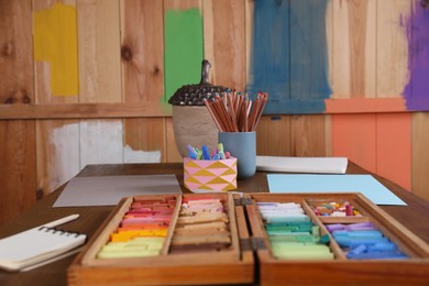 Blank sheets of paper, colorful chalk pastels and drawing pencils on wooden table indoors. Modern artist's workplace