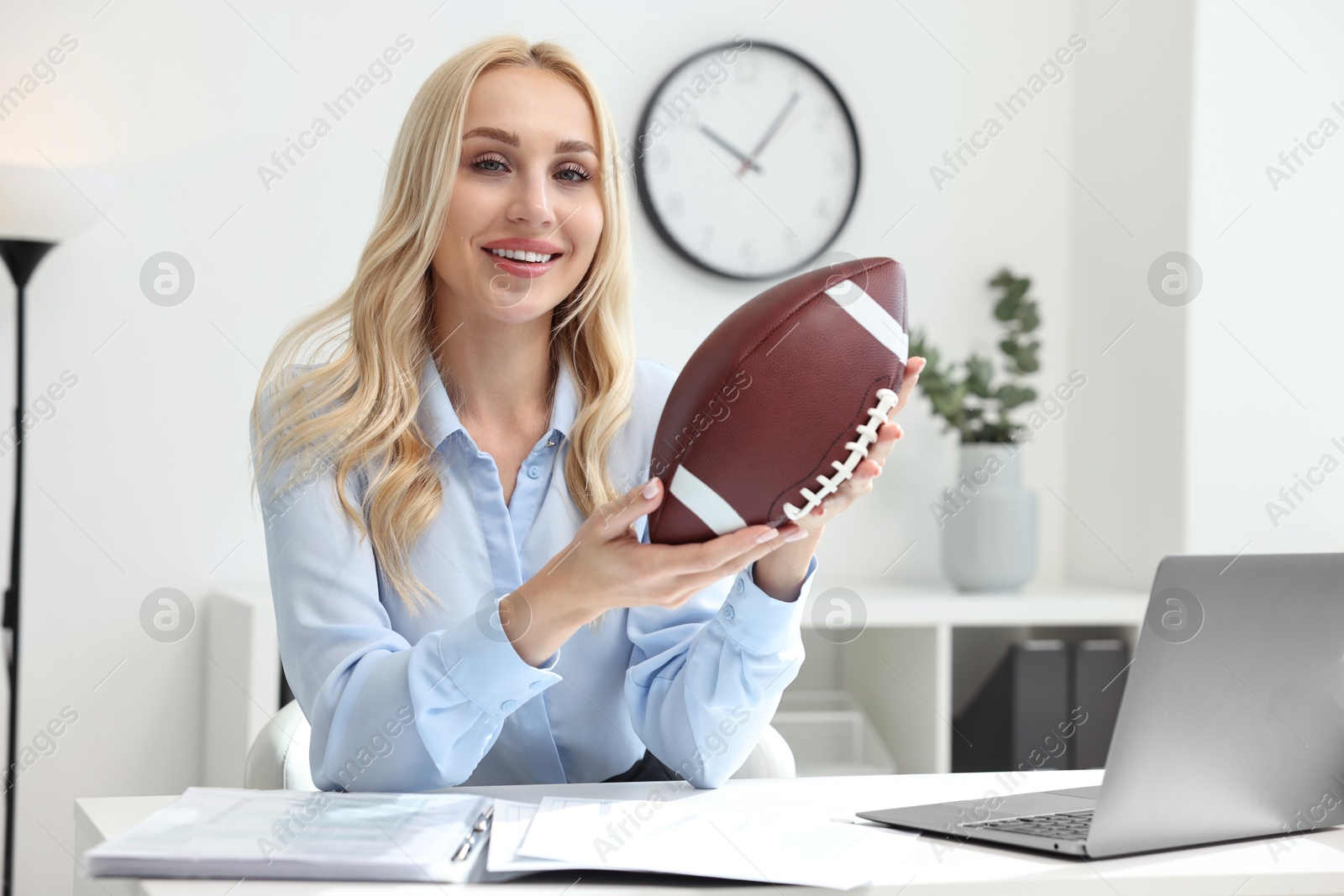 Photo of Happy woman with american football ball at table in office