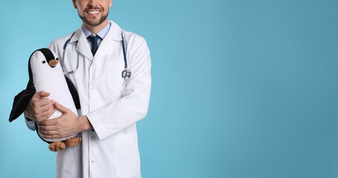 Photo of Pediatrician with toy penguin and stethoscope on light blue background, closeup. Space for text