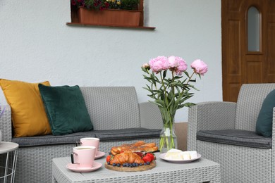 Photo of Morning drink, pastry, berries, cheese and vase with flowers on rattan table. Summer breakfast on terrace