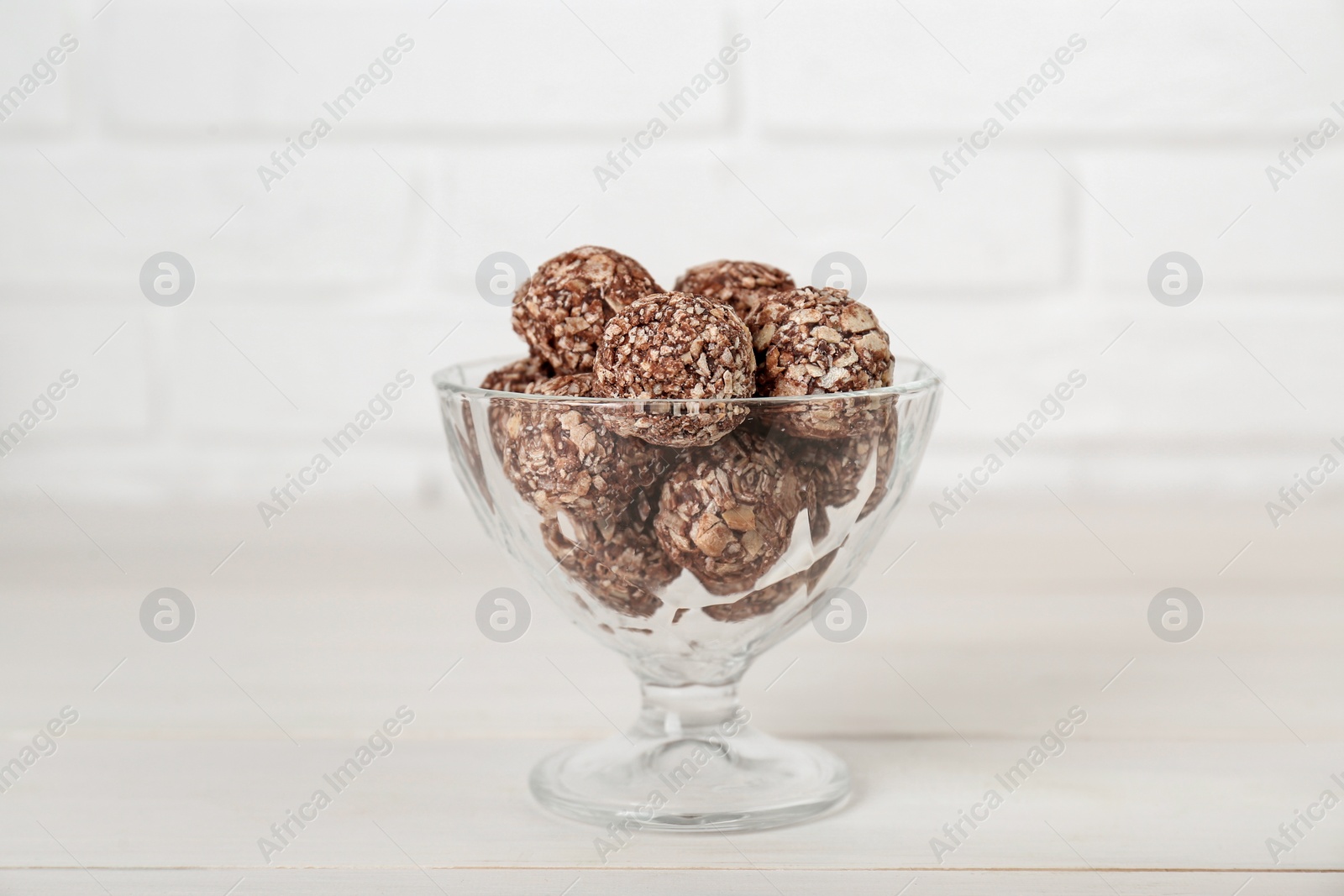 Photo of Glass dessert bowl of tasty chocolate balls on white wooden table, closeup