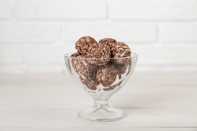 Glass dessert bowl of tasty chocolate balls on white wooden table, closeup