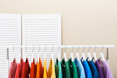 Photo of Rack with bright clothes in room. Rainbow colors