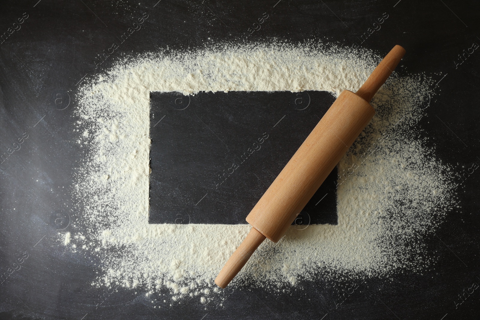 Photo of Flour and rolling pin on black table, top view