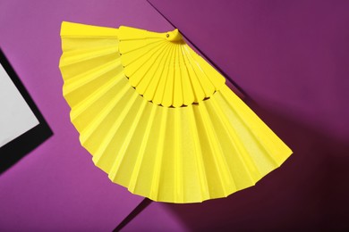 Photo of Folding yellow hand fan on purple background