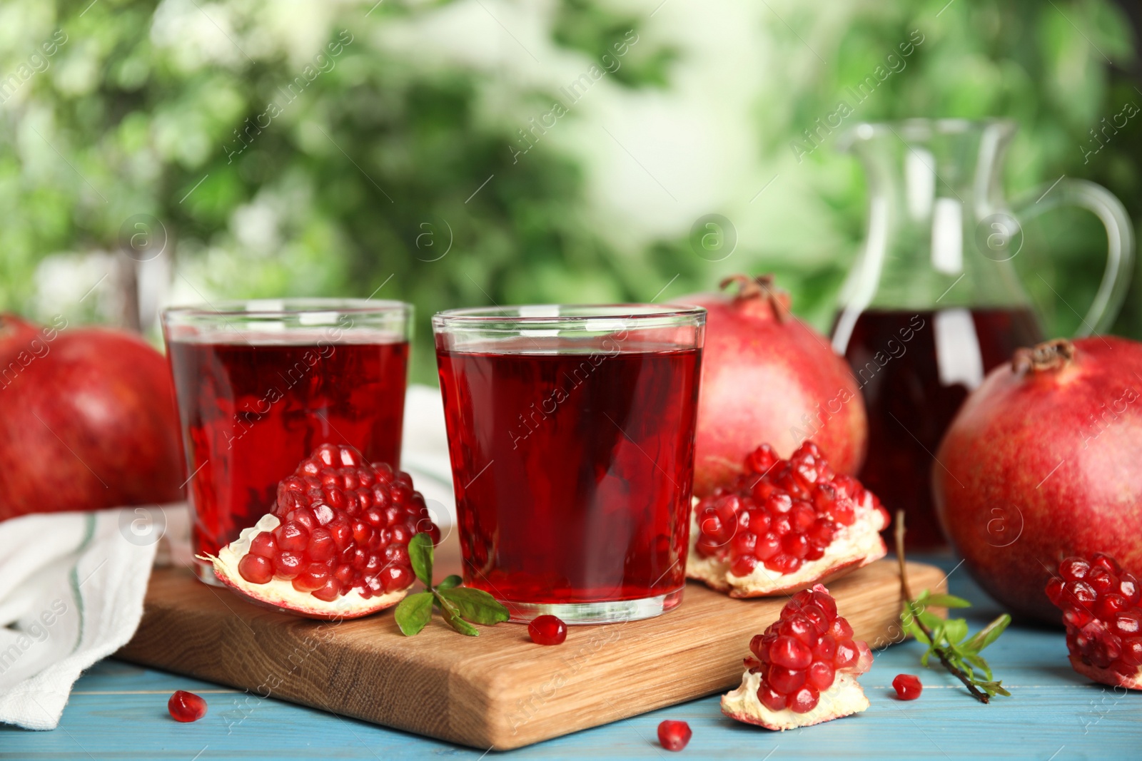 Photo of Pomegranate juice and fresh fruits on light blue wooden table outdoors