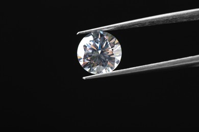 Photo of Tweezers with beautiful shiny diamond on black background, closeup. Space for text