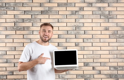 Photo of Young man with laptop on brick wall background