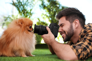 Photo of Professional animal photographer taking picture of beautiful Pomeranian spitz dog on grass outdoors