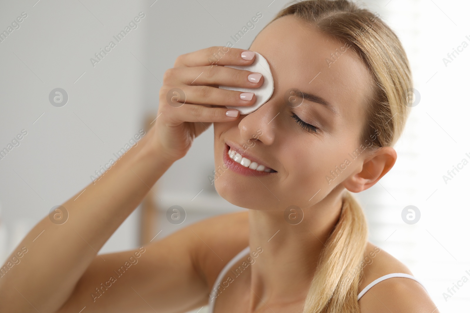 Photo of Smiling woman removing makeup with cotton pad indoors, closeup