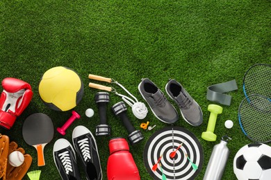 Photo of Different sport equipment and sneakers on green grass, flat lay. Space for text