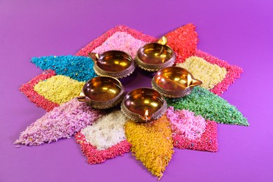 Diwali celebration. Diya lamps and colorful rangoli on purple background