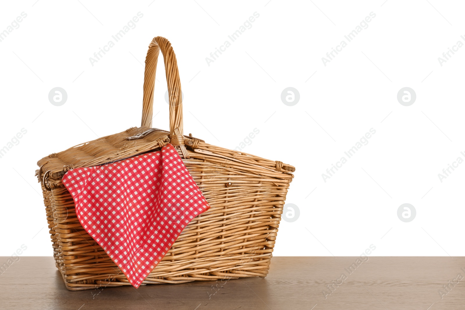 Photo of Closed wicker picnic basket with checkered tablecloth on wooden table against white background