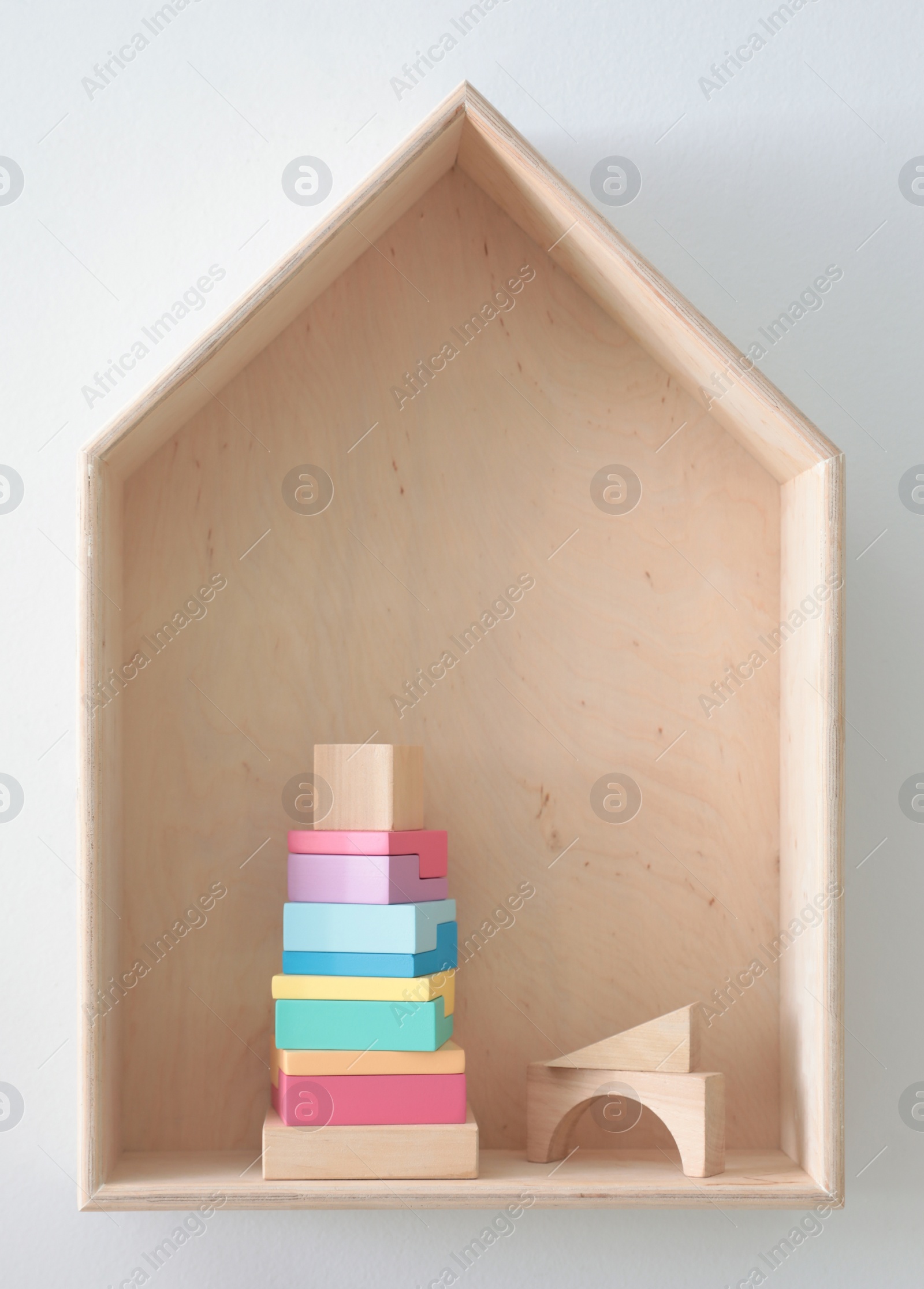 Photo of House shaped shelf with toys on white wall. Interior design