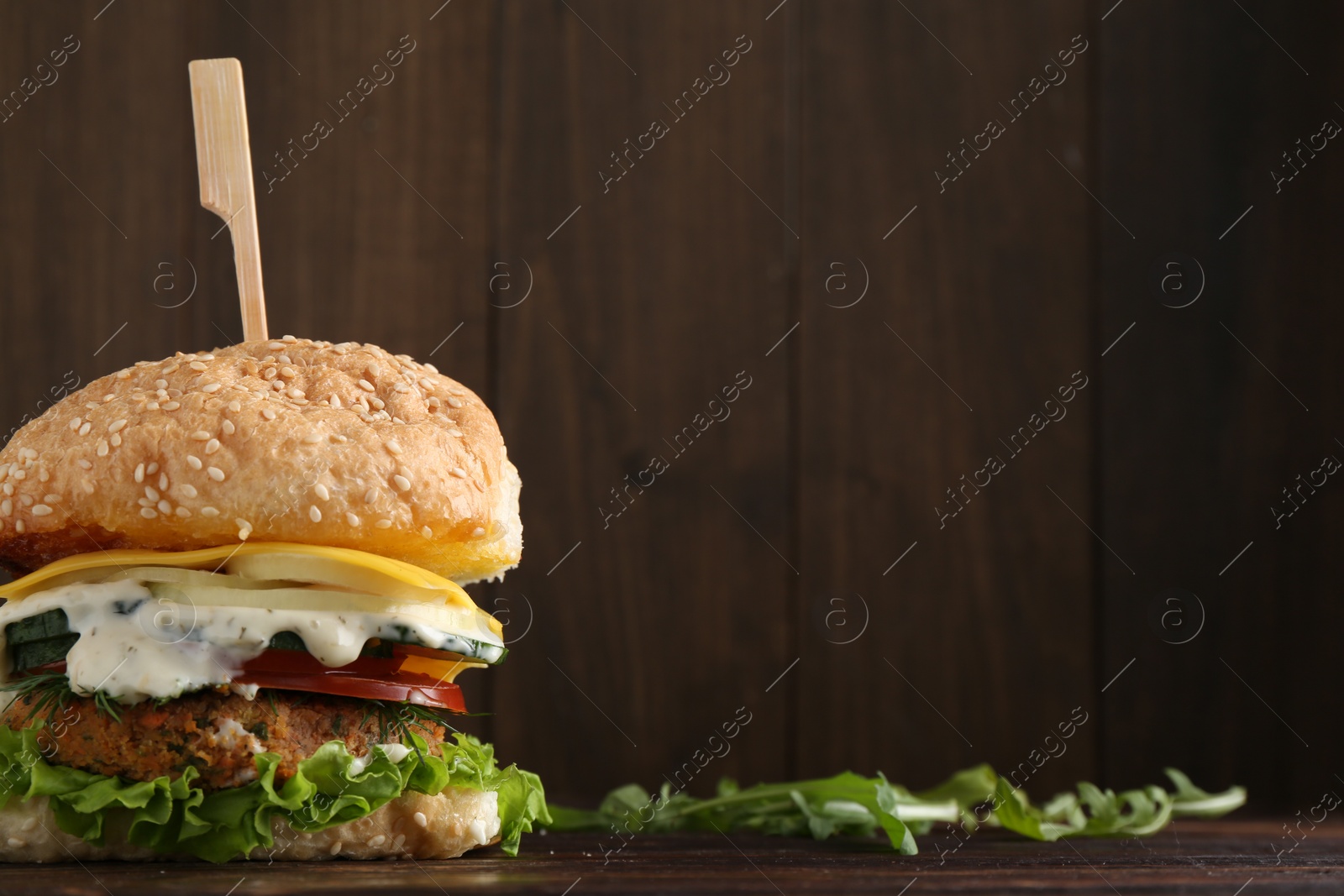 Photo of Delicious vegetarian burger and arugula on wooden table, space for text