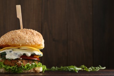 Photo of Delicious vegetarian burger and arugula on wooden table, space for text