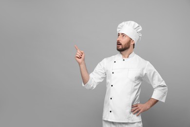 Photo of Mature chef pointing at something on grey background, space for text