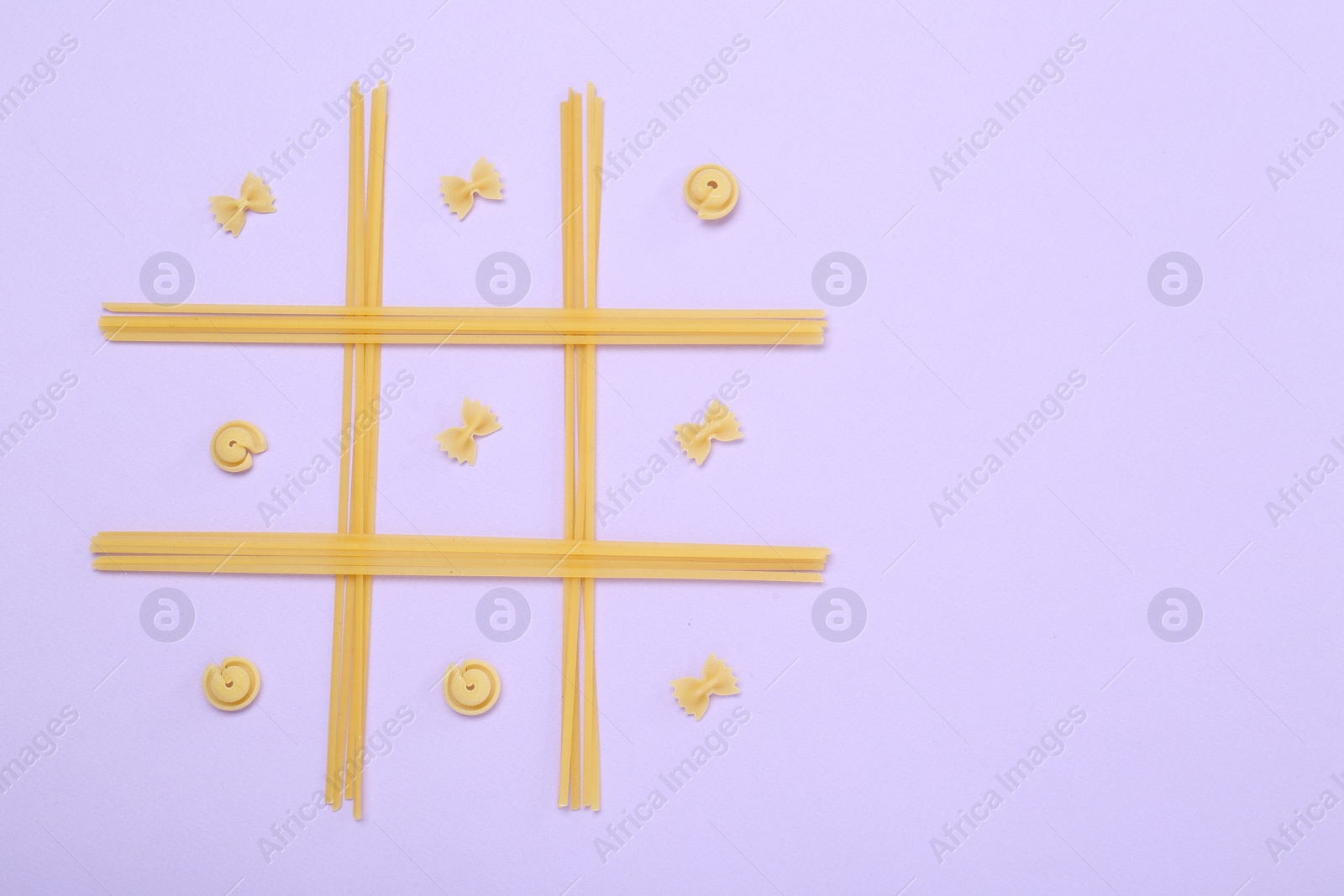 Photo of Tic tac toe game made with different types of pasta on lilac background, top view