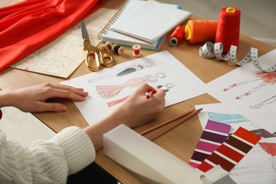 Photo of Fashion designer creating new clothes in sketchbook at wooden table, closeup