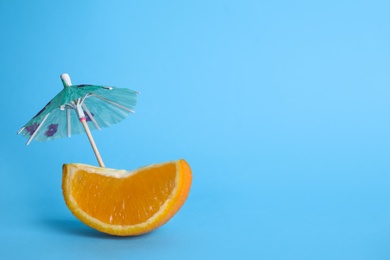 Photo of Slice of orange with cocktail umbrella on color background, space for text