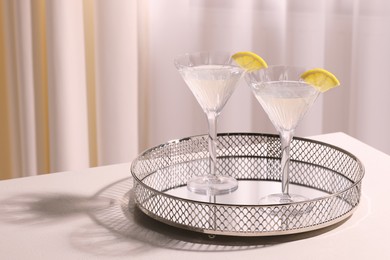 Tray with martini glasses of fresh cocktail and lemon slices on white table indoors. Space for text