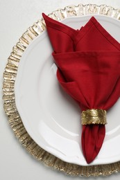 Photo of Plate with red fabric napkin and decorative ring on white table, top view