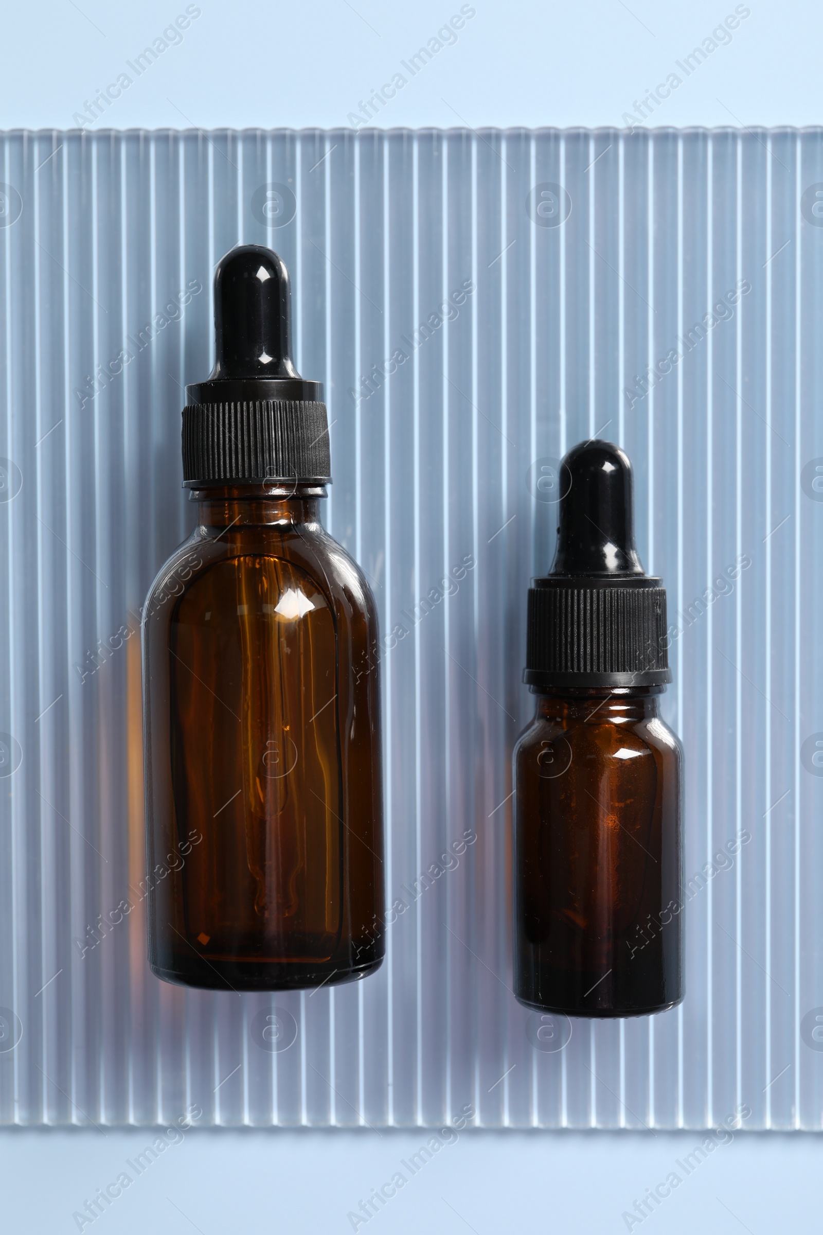 Photo of Bottles of cosmetic serum on light blue background, top view