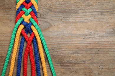 Photo of Top view of braided colorful ropes on wooden background, space for text. Unity concept