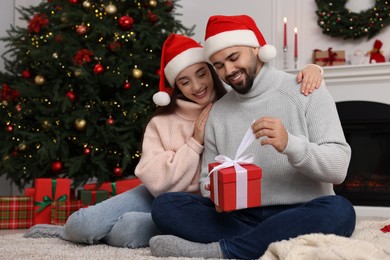 Happy woman in Santa hat presenting Christmas gift to her boyfriend at home