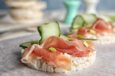Photo of Puffed rice cake with prosciutto and cucumber on parchment paper, closeup