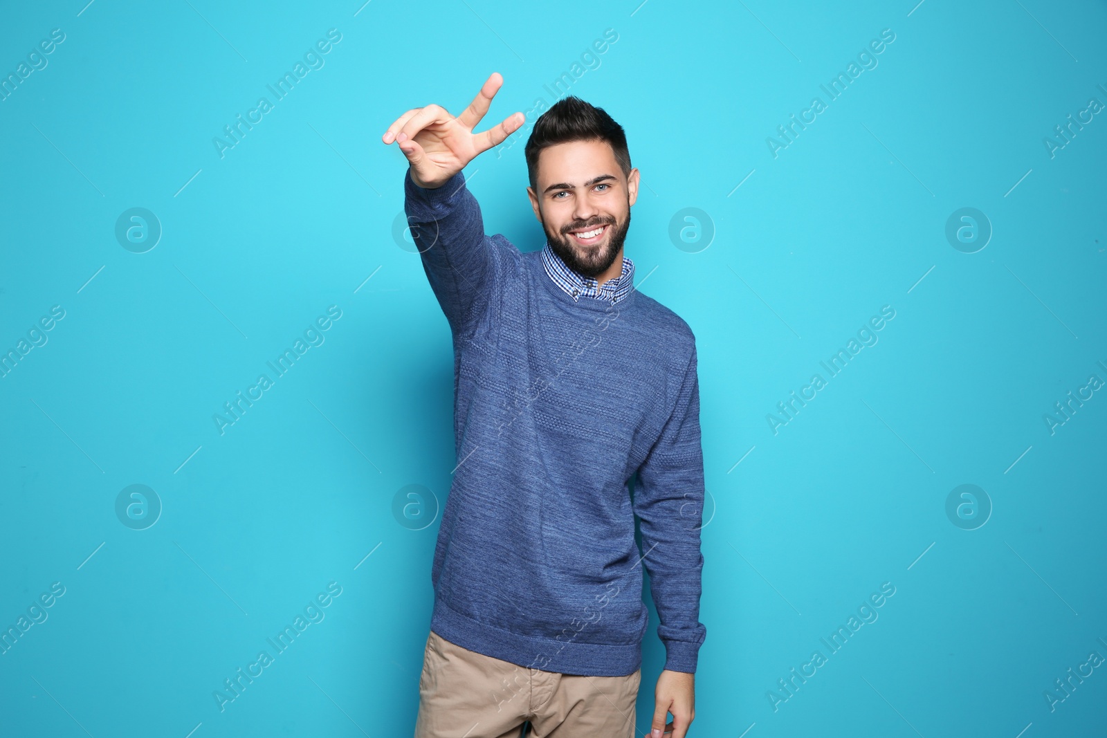 Photo of Happy young man showing victory gesture on color background