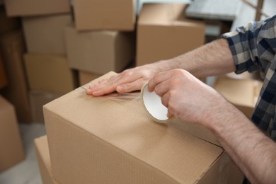 Photo of Man taping cardboard box indoors, closeup. Moving day