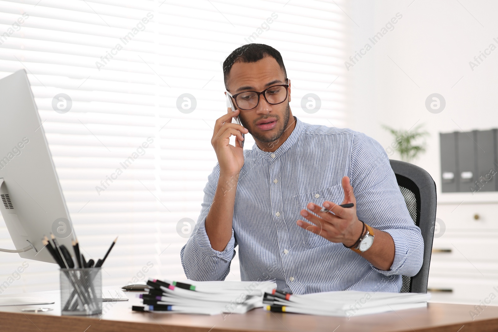 Photo of Man talking on phone while working with documents at wooden table in office
