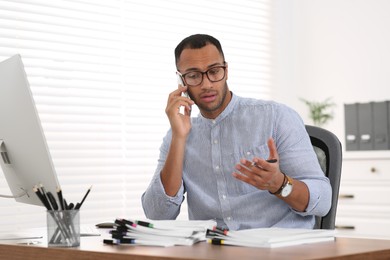 Photo of Man talking on phone while working with documents at wooden table in office