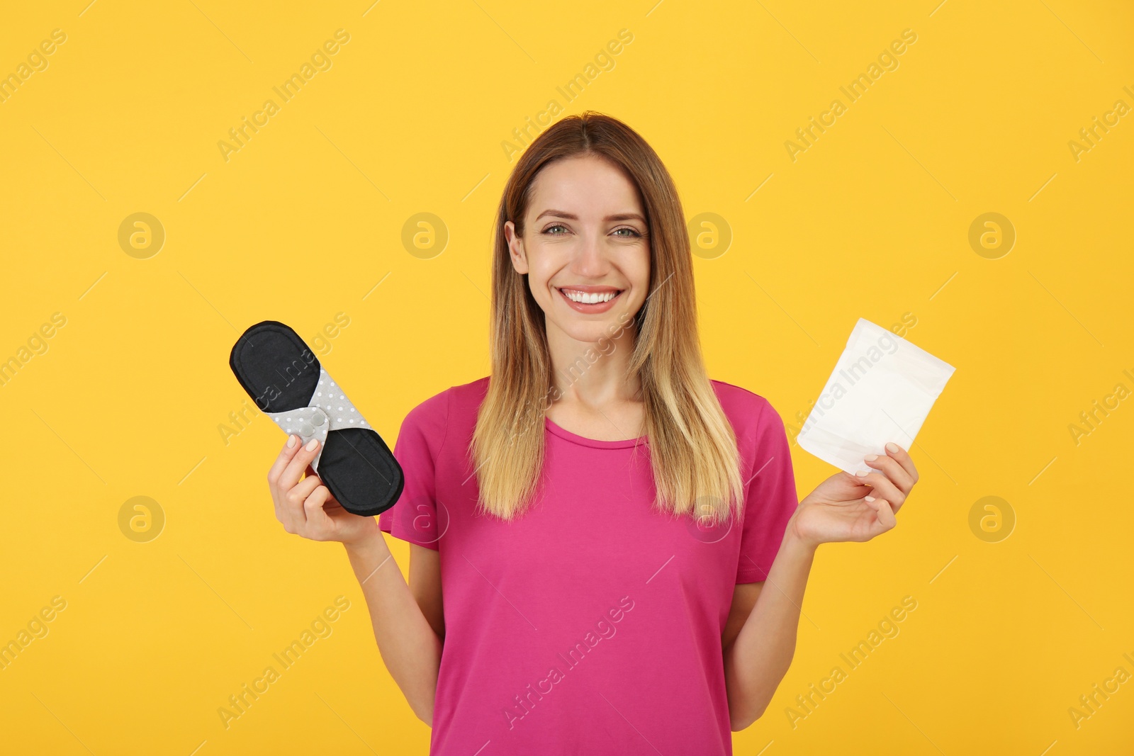 Photo of Happy young woman with disposable and reusable cloth menstrual pads on yellow background