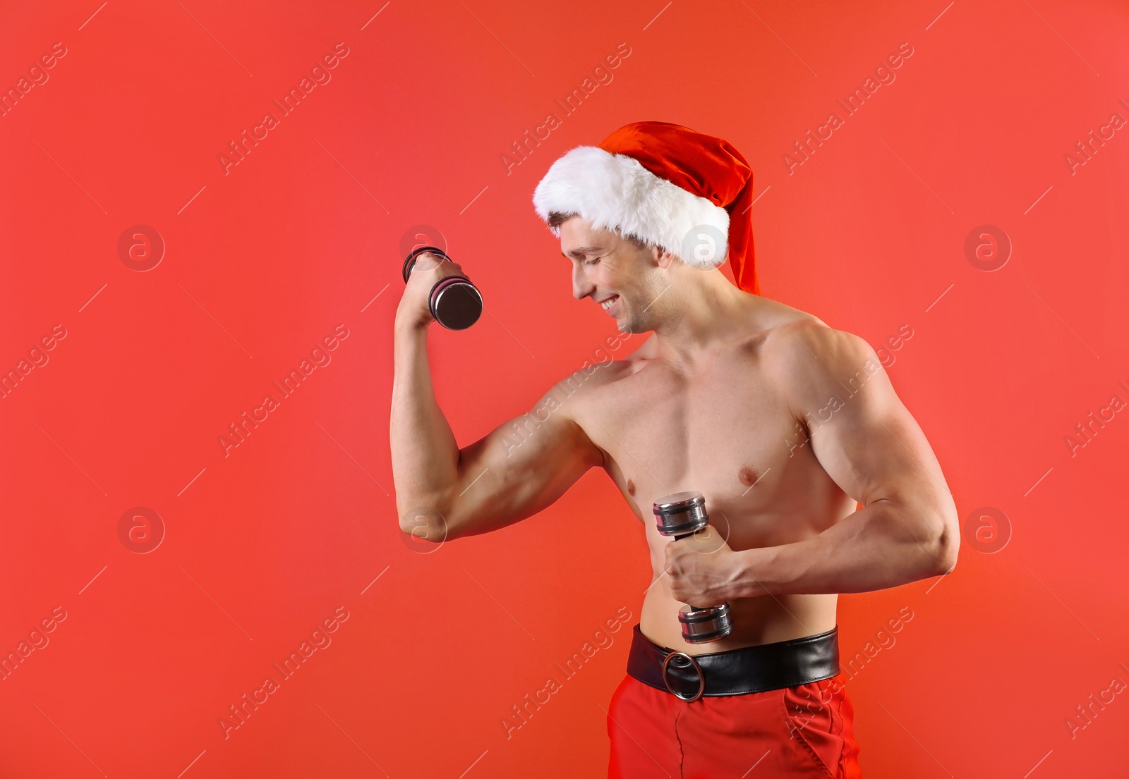 Photo of Young muscular man in Santa hat with dumbbells on color background