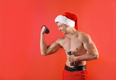 Photo of Young muscular man in Santa hat with dumbbells on color background