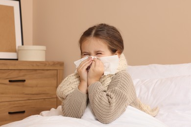 Photo of Girl blowing nose in tissue on bed in room. Cold symptoms
