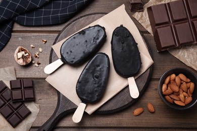 Photo of Delicious glazed ice cream bars, chocolate and nuts on wooden table, flat lay