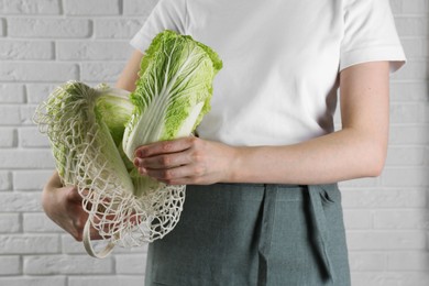 Woman holding fresh Chinese cabbages near white brick wall, closeup