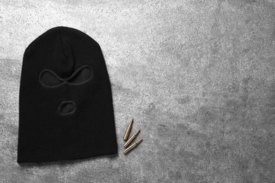 Photo of Black knitted balaclava and bullets on grey table, flat lay. Space for text