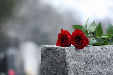 Photo of Red roses on grey granite tombstone outdoors. Funeral ceremony