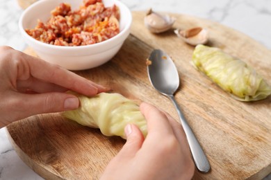 Woman preparing stuffed cabbage roll at table, closeup